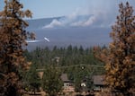 A firefighting aircraft flies over the southeast part of the Akawa Butte Fire, near a neighborhood on the northern outskirts of Sisters, Ore., on a windy afternoon on July 25, 2026.