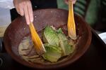 Two hands mix Romaine leaves with other ingredients in a bowl to prepare a Caesar salad.