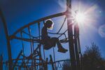 Little girl with curly hair sits on top of a playground jungle gym.
