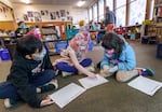 Students sit together on the floor of a classroom wearing face masks and looking at worksheets.