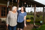 A woman and her grandmother embrace in front of a house.