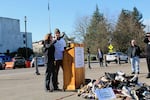 Gov. Brown stands with man at lectern and throws a shoe onto a pile of shoes