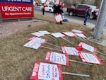 Picket signs with messages like "Support St. Charles Respiratory Therapy" lie on the grass outside St. Charles Bend Medical Center, near a hospital sign that reads "Urgent Care."
