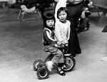 In this image from 1975, two Vietnamese refugees play with a tricycle at their temporary shelter in the Mount Angel beer hall.