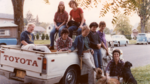 A group of women stands in and around a Toyota pickup truck parked on a residential street.