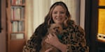 A woman in a cheetah-print fur coat smiles and holds a small dog.