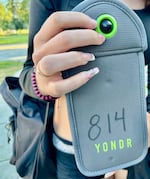 Ava McCandless, a junior at Grant High School, shows her Yondr cellphone pouch out front of the Northeast Portland school on Wednesday, Aug. 28, 2024. Students will lock their phones, earbuds and smartwatches in the pouches at the start of the school day and get them opened at the end.