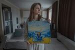 Alona Serdiuk, 23, an IDP from Komysh Zoria, Zaporizhzhia region holds her painting in Ukrainian's flag colors at parents' home in Zaporizhia.