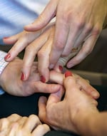 five hands, intertwined together as three people use protactile language to talk. one person is wearing red fingernail polish.