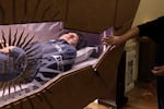 A person reaches out to the remains of Carlo Acutis, which have rested since April 6, 2019, at a church in Assisi, Italy. The teenager's face and hands are reconstructed with silicone.