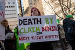 A woman holds sign written in black, green and red that reads, "Death by claim denial = negligent homicide."