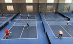 Nine players in a bright blue pickleball court at Jumbo's Pickleball.