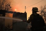 A firefighter waters down a home after the Eaton Fire burns in Altadena, Calif., Thursday, Jan. 9, 2025.