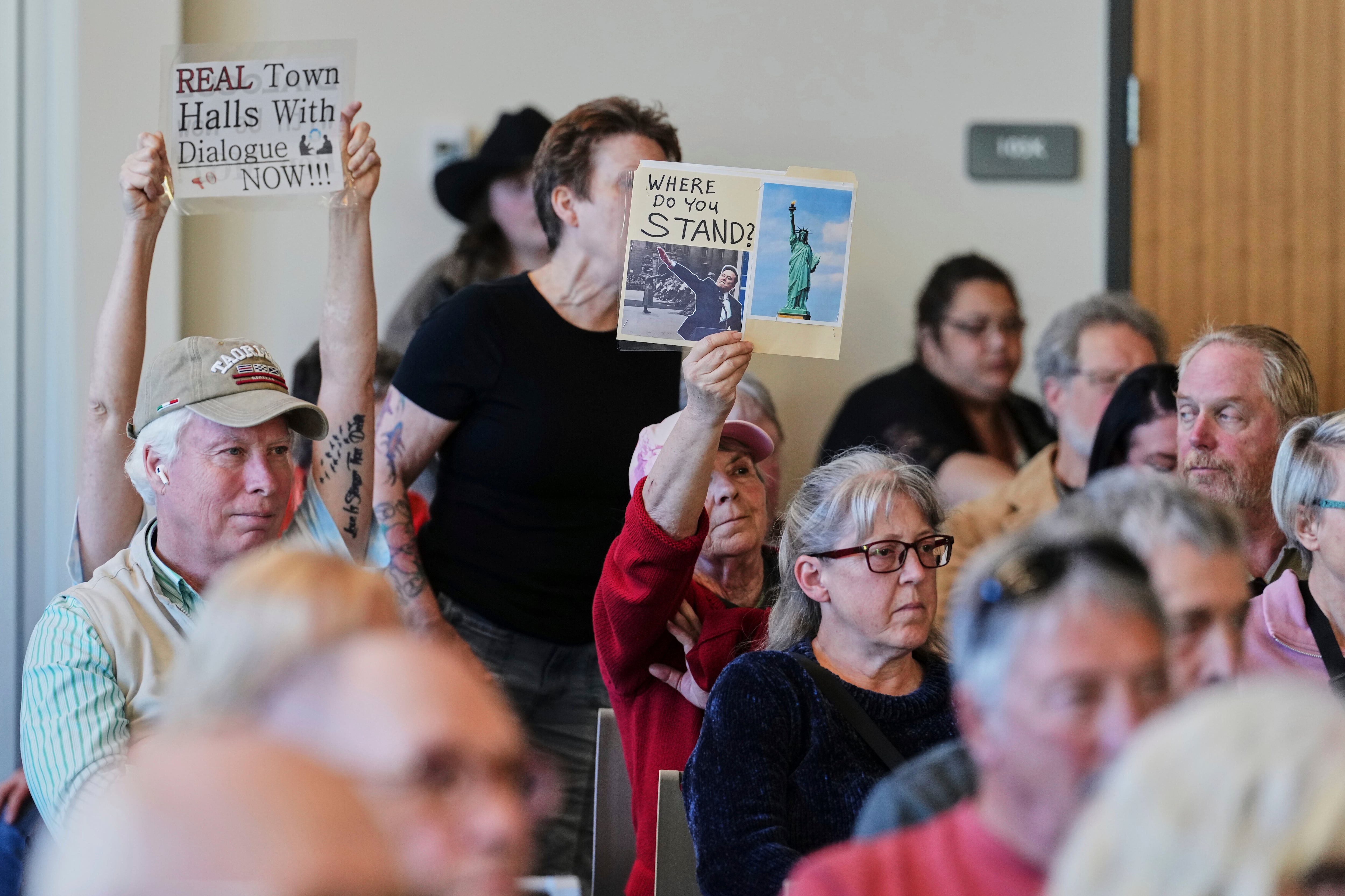 A woman in red holds up a sign during the town hall event with Rep. Marie Gluesenkamp Perez.