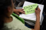 FILE - Kaori Eder, pens "children over politics” on a sign board during a Portland Public Schools board meeting at the Dr. Matthew Prophet Education Center in Portland, Ore., in April 2026.
