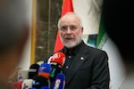 Iran's parliament speaker, Mohammad Bagher Ghalibaf, stands in front of a cluster of microphones from various news outlets as he speaks during a commemoration ceremony for late Iranian Supreme Leader Ali Khamenei in Karbala, Iraq, on August 20. He is wearing a black shirt and black suit jacket.
