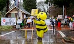 A person in an inflatable bee suit and others hold signs opposing immigration enforcement in the rain.