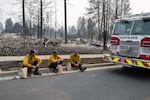 Three members of the Spokane Fire Department sit on a curb in front of burned out residential homes in the Balboa neighborhood of Spokane, Wash., on August 2, 2026.