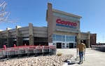 A lone shopper pushes a cart toward the entrance of a Costco warehouse on a cloudless day.