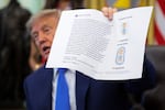 President Donald Trump holds up a printout of one of his Truth Social posts before signing an executive order that calls for changing the childhood vaccine schedule on August 10, 2026. He is facing a lawsuit over a service offering early access to his Truth Social feed for up to $100,000 a month.