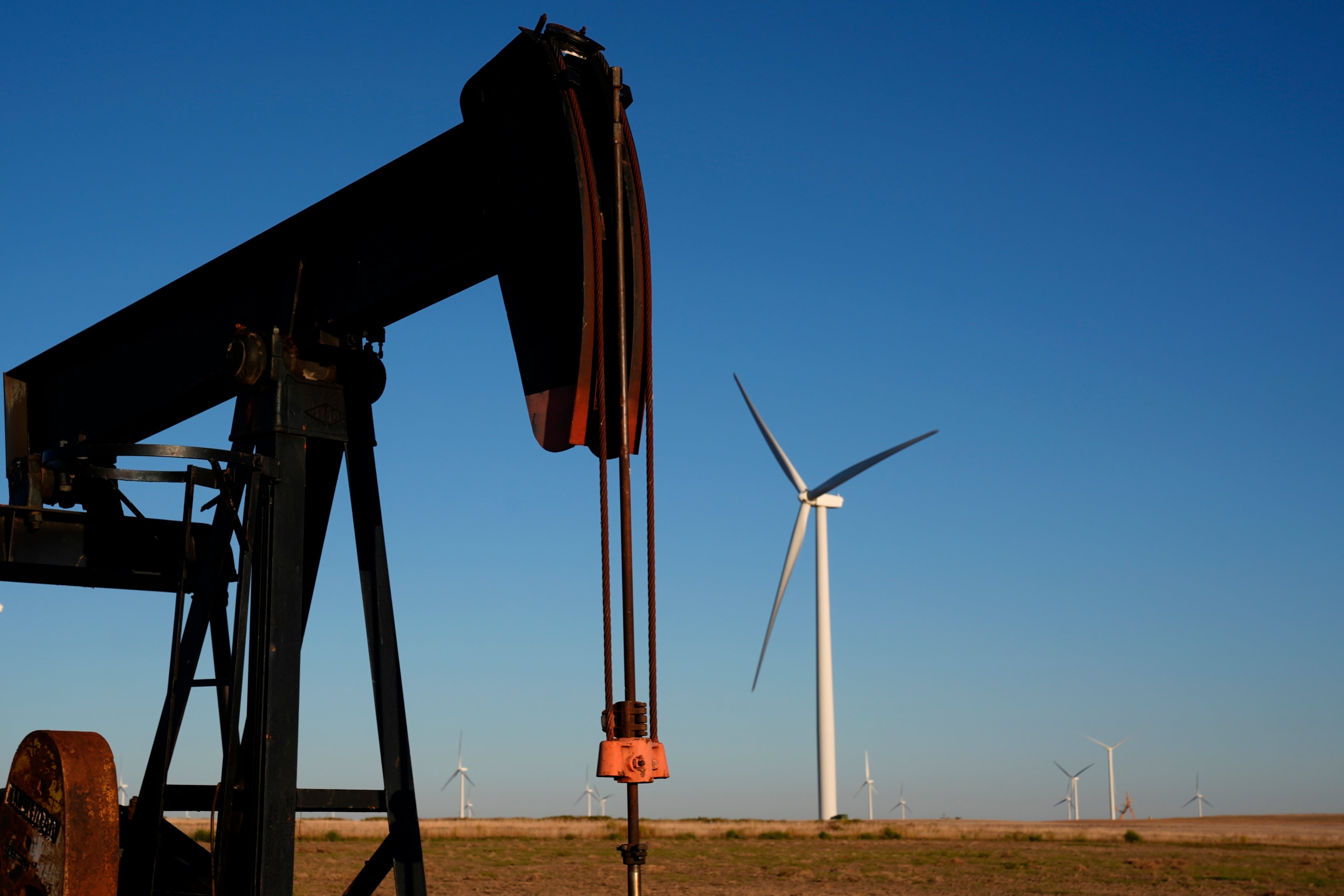 FILE - Pumpjacks operate in the foreground while a wind turbines at the Buckeye Wind Energy wind farm rise in the distance Monday, Sept. 30, 2024, near Hays, Kan.