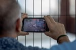 At one of the perimeter fences, a spectator films a large outdoor screen showing the race.