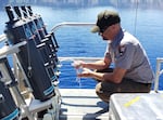 An aquatic biologist collects a water sample from special sampling bottles that are lowered into Crater Lake at different depths.