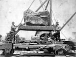 Workers load a boulder on a rail cart.
