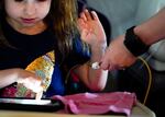 Scarlett Rasmussen, 8, watches a video on her tablet as mother, Chelsea, administers medication while they get ready for school, Wednesday, May 17, 2023, at their home in Grants Pass, Ore. Chelsea, has fought for more than a year for her daughter, Scarlett, to attend full days at school after starting with a three-day school week. She says school employees told her the district lacked the staff to tend to Scarlett’s medical and educational needs, which the district denies. Scarlett is nonverbal and uses an electronic device and online videos to communicate, but reads at her grade level. She was born with a genetic condition that causes her to have seizures and makes it hard for her to eat and digest food, requiring her to need a resident nurse at school.