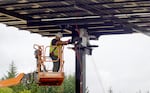 A worker bolting a solar pane on an elevated beam at Our Table Cooperative farm in Sherwood, Ore., on Sept. 12, 2024.