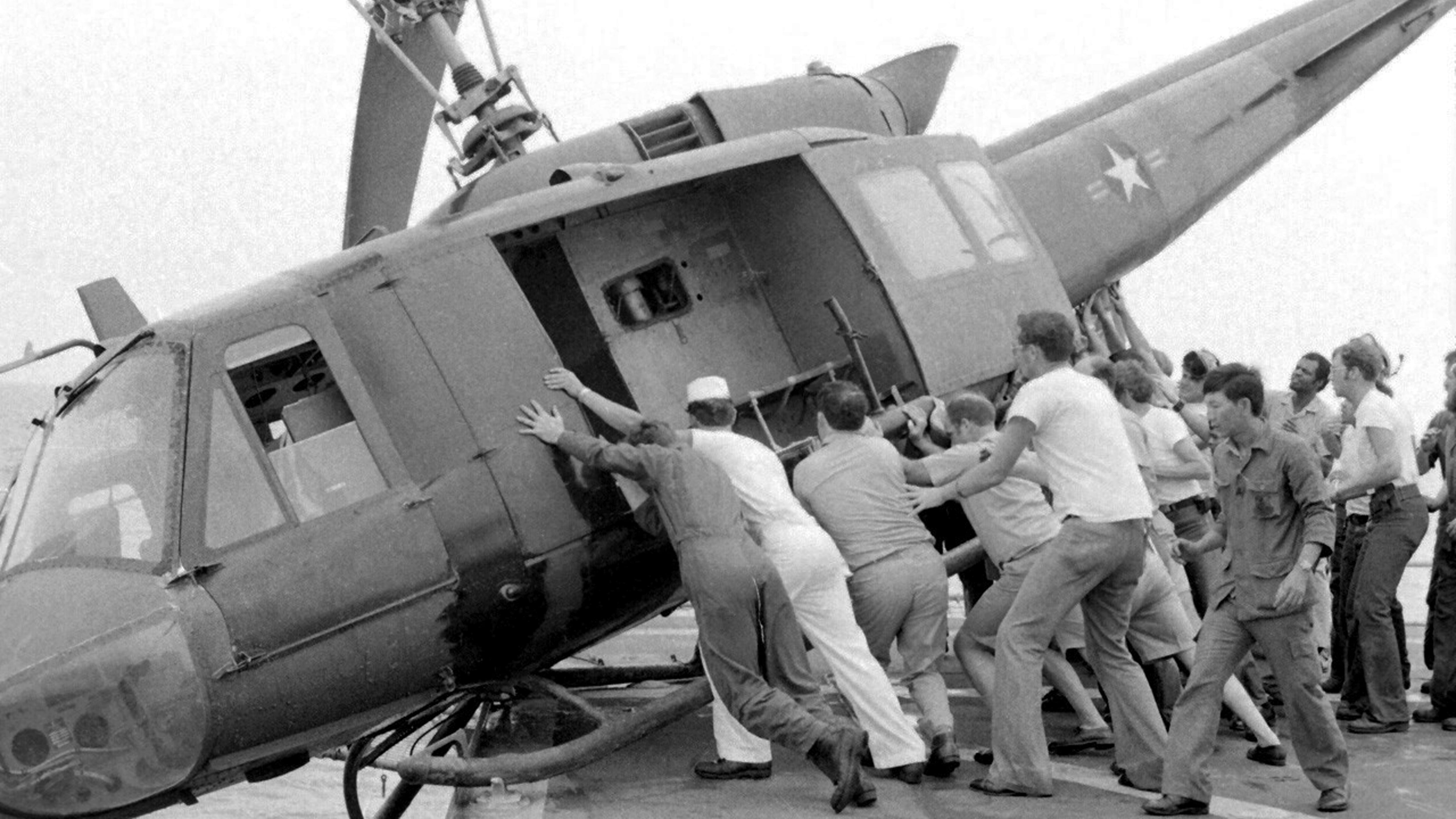 U.S. Navy personnel struggle to push an army Huey helicopter off the deck of a U.S. Navy carrier to make room for more refugee flights on April 29, 1975.