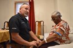 Shane McMahon, a paramedic, kneels beside Stephanie Joseph, 91, who is sitting down in her home.