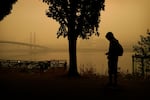 A person rides a skateboard along the Willamette River as smoke from wildfires partially obscures the Tilikum Crossing Bridge, Saturday, Sept. 12, 2020, in Portland, Ore.