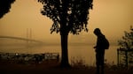 A person rides a skateboard along the Willamette River as smoke from wildfires partially obscures the Tilikum Crossing Bridge, Saturday, Sept. 12, 2020, in Portland, Ore.
