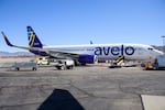 An Avelo Airlines jet on the tarmac at Hollywood Burbank Airport in 2021. The plane has a white fuselage with the word "avelo" in lowercase blue letters on its side. The plane's tail has the airline's blue logo on it.