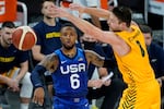 A basketball player in a blue uniform labeled USA 6 has just thrown a basketball, which is seen moving through the air as another player wearing yellow reaches for the ball.