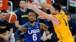 A basketball player in a blue uniform labeled USA 6 has just thrown a basketball, which is seen moving through the air as another player wearing yellow reaches for the ball.