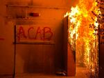 A building is show on fire. The graffiti "ACAB" is visible.