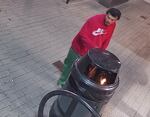 A man in a red sweater near a trash can in which there is a fire.