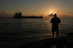 FILE - An oil tanker passes at sunrise while a man fishes in Port Aransas, Texas, Aug. 9, 2025.