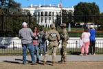 FILE - People talk with National Guard soldiers on the Ellipse, with the White House in the background, Oct. 17, 2025, in Washington.