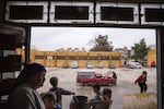 Sabah Hassan Bero, 54, (left) stands at the entrance to a vacant school as children play. A man looks under the hood of his red pickup truck in the courtyard.