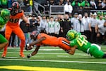 An Oregon State football player in an orange uniform lunges into the end zone as he is tackles by an Oregon football player in a green uniform.