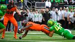An Oregon State football player in an orange uniform lunges into the end zone as he is tackles by an Oregon football player in a green uniform.