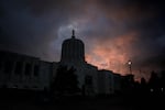 The Oregon Capitol forms a dark silhouette against a pink and blue sky with gray clouds.