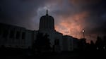 The Oregon Capitol forms a dark silhouette against a pink and blue sky with gray clouds.