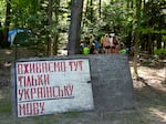 The camp is conducted in Ukrainian, and scouts are publicly rated on their language effort. This sign reads "Here We Use Only The Ukrainian Language," and behind it, older campers gather for singing practice.