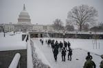 In this photo, members of law enforcement in uniform walk on snowy ground toward the entrance of the U.S. Capitol Visitor Center. The Capitol dome rises in the background.