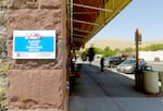 A bright blue sign that states "SUPPORT MCHD AMBULANCE SERVICE" hangs on a stone wall. In the background, a woman sweeps the sidewalk in front of Murray's Drug.