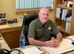 A man in law enforcement clothes sites at a desk.